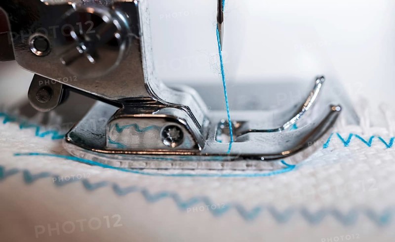 Close-up of sewing machine needle with blue thread sewing on a white fabric