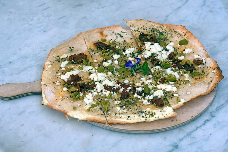 Flammkuchen with olives dried tomatoes and feta cheese on a wooden board