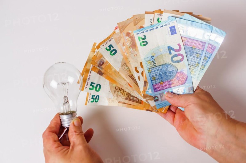 Woman holding banknotes in one hand and a light bulb in the other concept of light prices