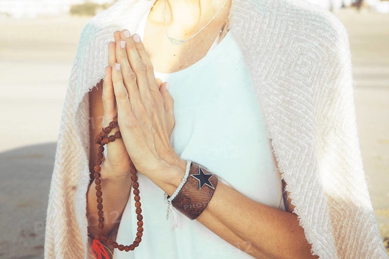 Close up of a woman clasping hands while holding a japa mala outdoors