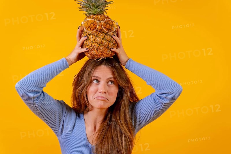 Woman with a pineapple in sunglasses in a studio on a yellow background