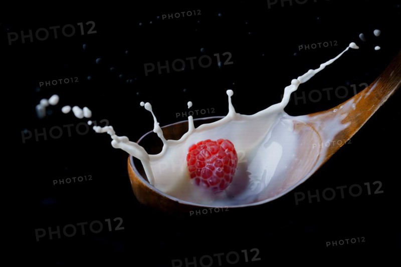 Fresh raspberry splashing milk on a wooden spoon