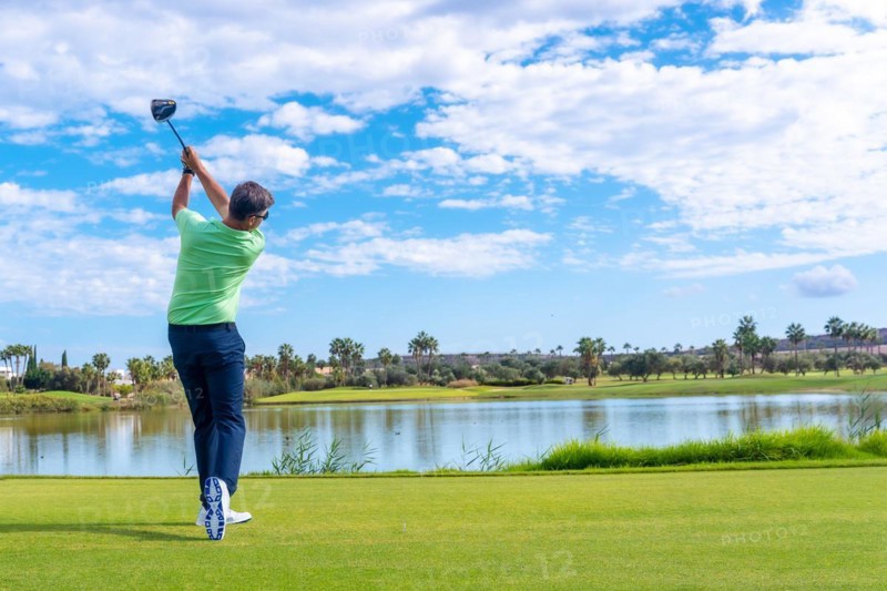 Male golf player on professional golf course. Golfer hitting the ball with driver stick next to a lake