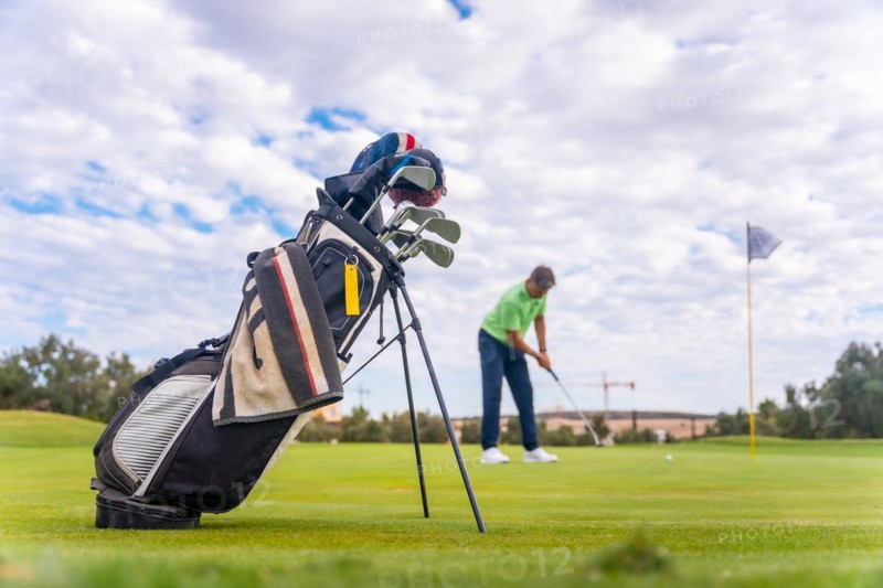 Caucasian professional golf player on the green preparing for the shot next to the fairway carrying bags