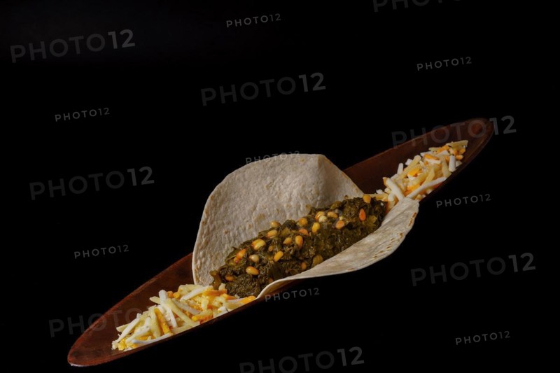 Taco with spinach and pine nuts and various types of cheeses as garnish and black background