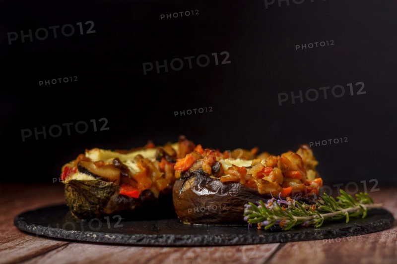 Foreground eggplant stuffed with meat and vegetables covered with bechamel sauce on a black slate on a wooden table