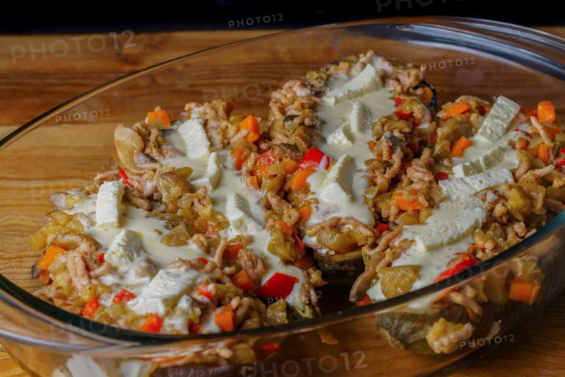 Eggplants stuffed with meat and vegetables covered with bechamel sauce on a glass tray on a wooden table