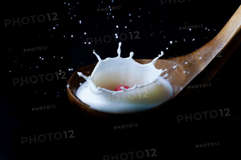 Fresh raspberry splashing milk on a wooden spoon
