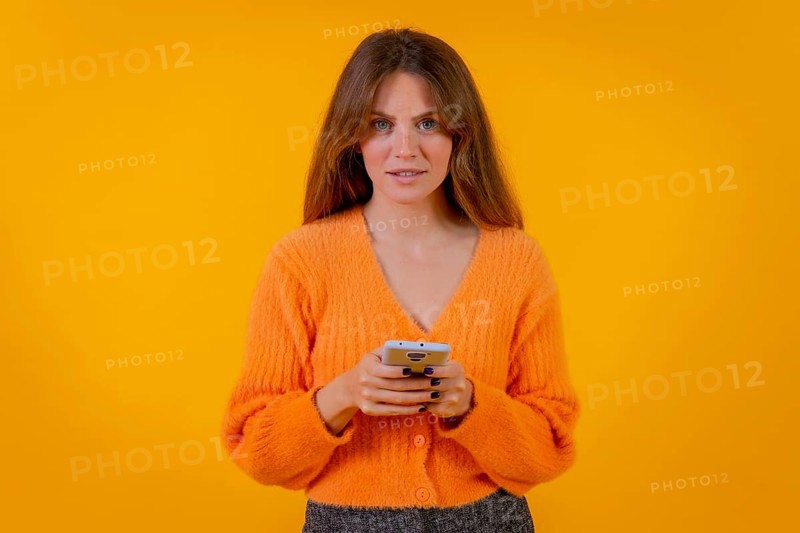 A woman looking at things on the internet on the mobile phone on a yellow background