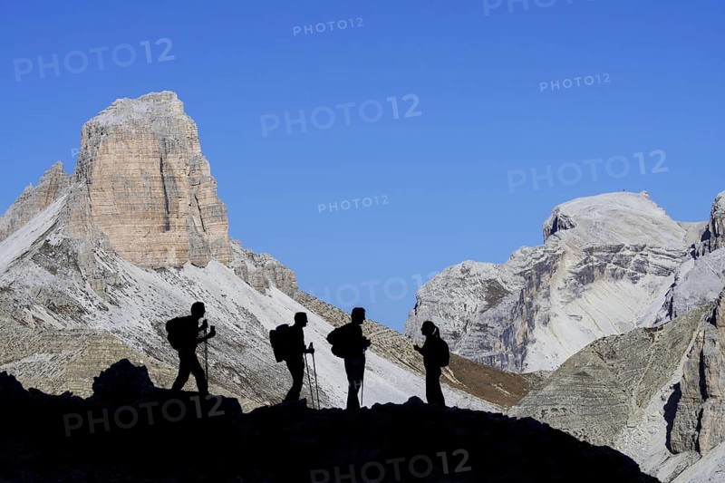 Four mountain climbers silhouetted against Torre dei Scarperi