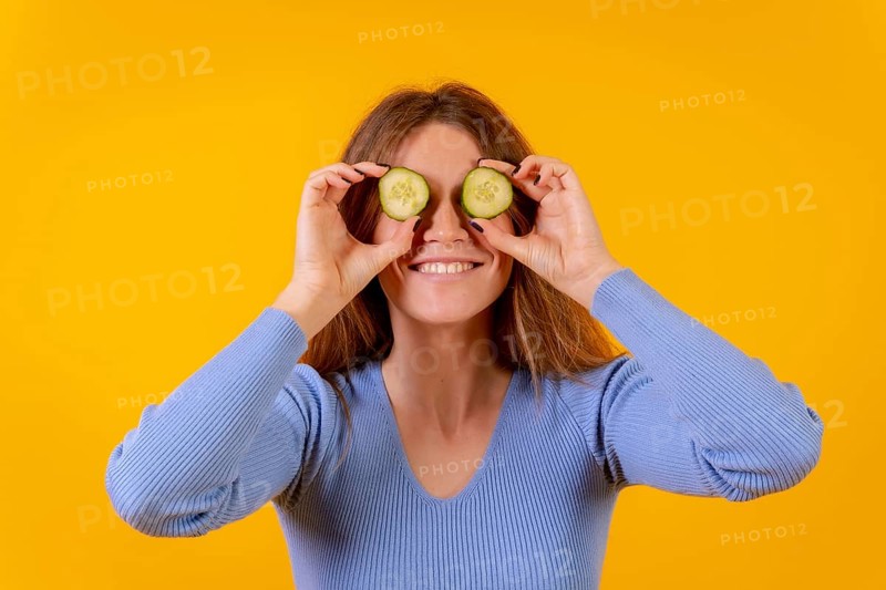 Vegan woman with cucumber slices on her eyes on a yellow background