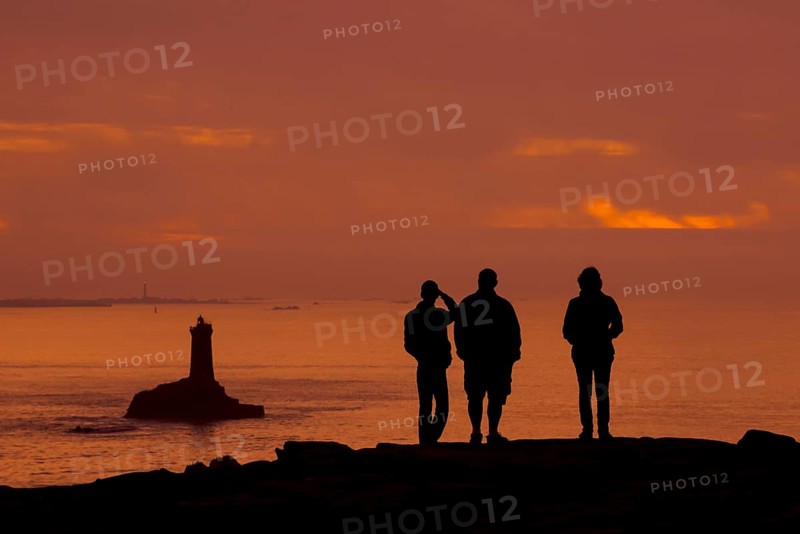 Tourists watching the lighthouse La Vieille in the strait Raz de Sein silhouetted against sunset at the Pointe du Raz