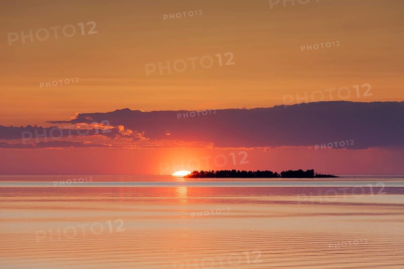 Sunset with sun setting behind silhouetted island in Lake Vaenern
