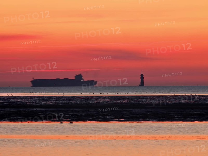 Container freighter on the Outer Weser with lighthouse in the evening light
