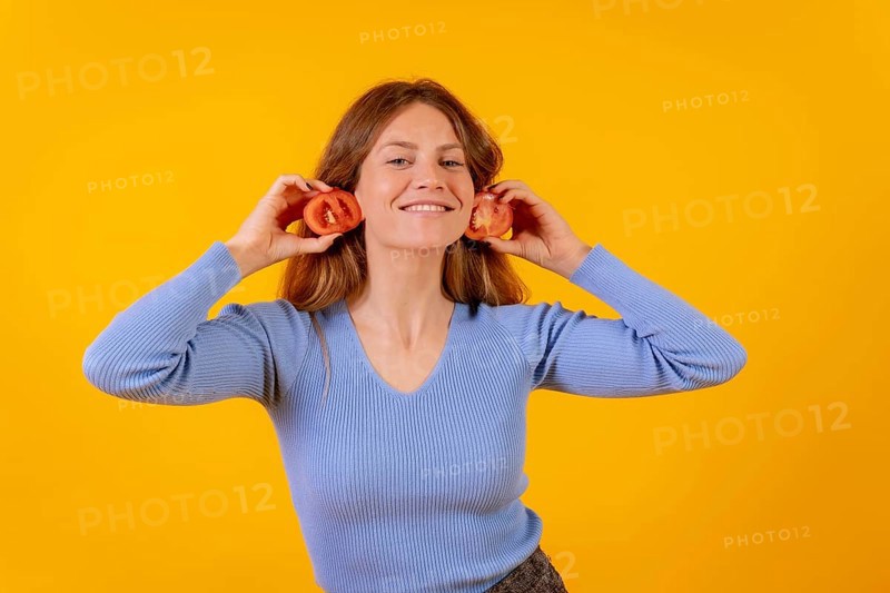 Vegan woman smiling with earrings tomato slices on a yellow background
