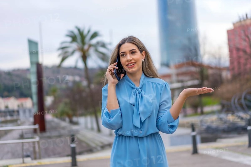 Blonde woman in blue dress smiling talking on the phone walking in the city