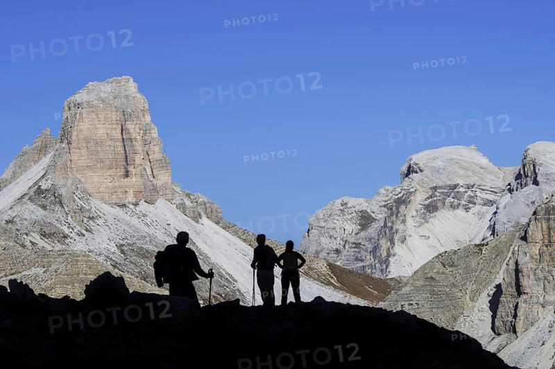 Three mountain walkers silhouetted against Torre dei Scarperi