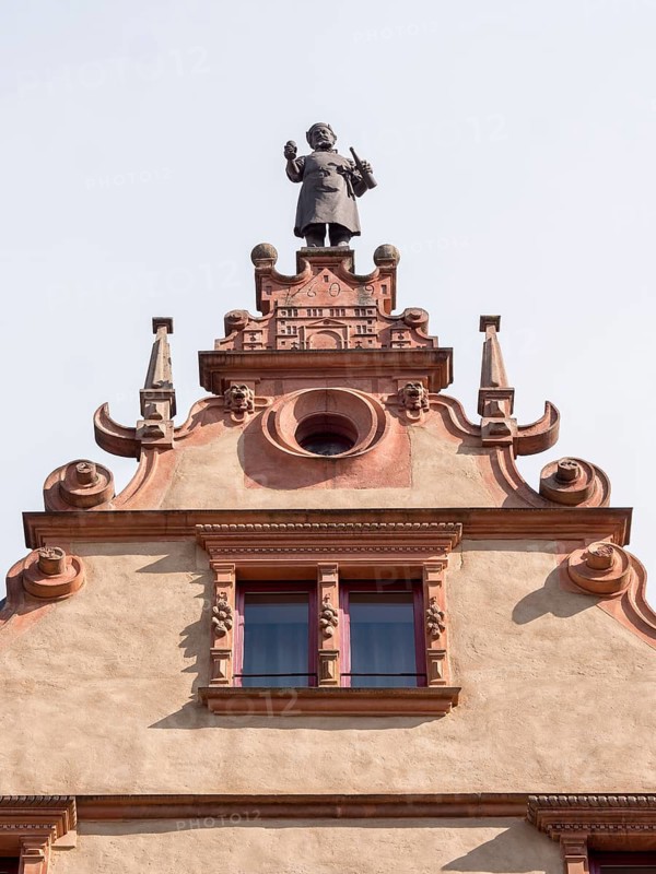 The top of a medieval building La Maison des Tetes with a male statue at the top of Rue des Tetes