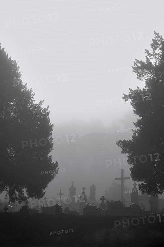 Silhouetted tombs and crosses at graveyard in the mist