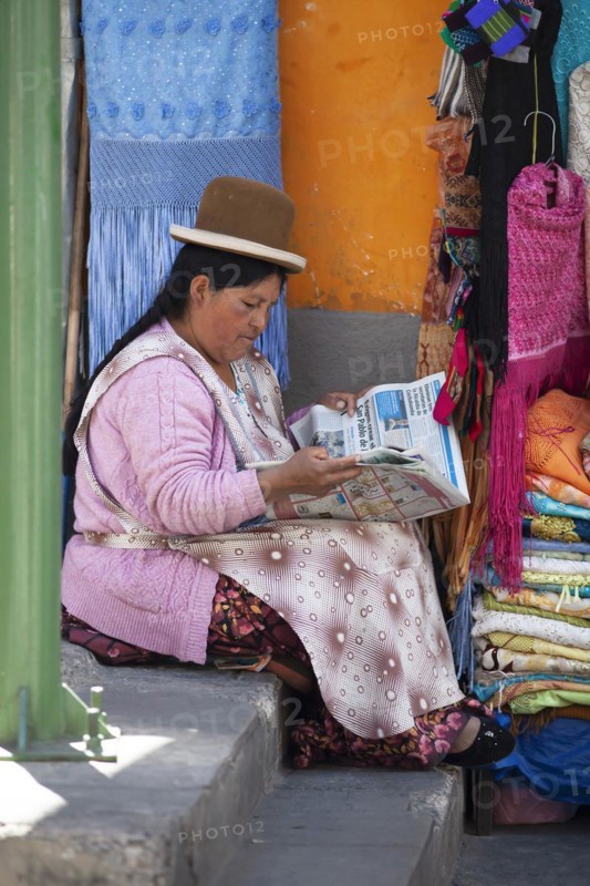 Bolivian woman wearing a traditional hat reading a newspaper