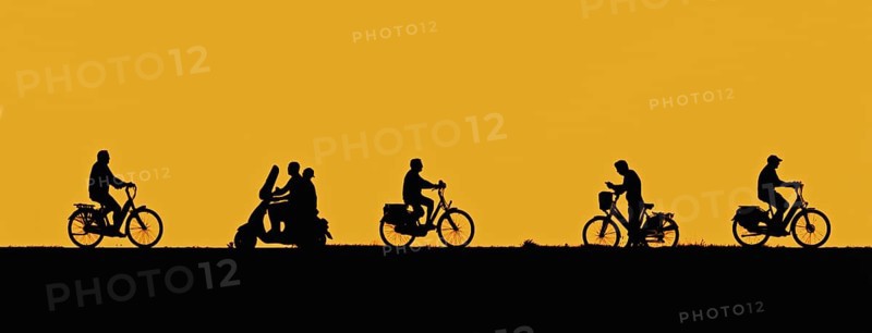 Motor scooter riding past cyclists and man on bicycle checking his smartphone silhouetted against orange sunset sky in summer