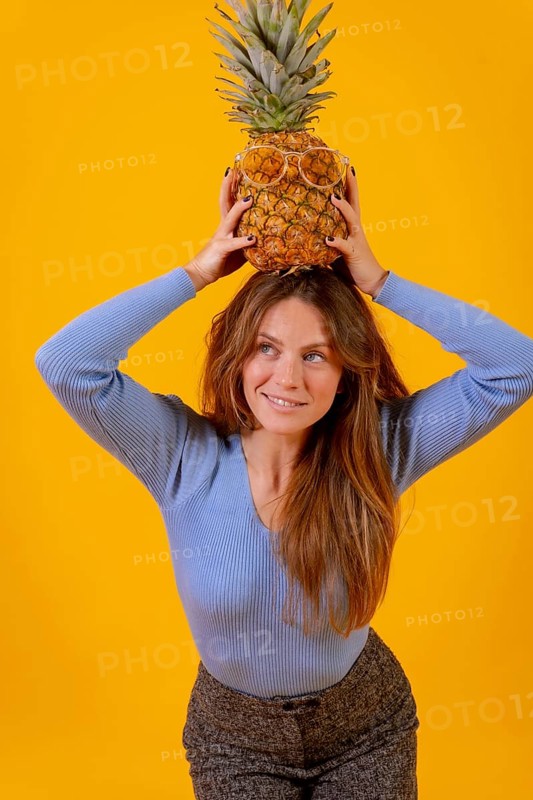 Woman with a pineapple in sunglasses in a studio on a yellow background