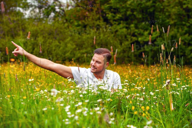 Man sitting in a field of flowers with arm outstretched