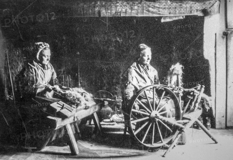 Early 20th century photograph showing two old female home spinners using wooden spinning wheel and hackle