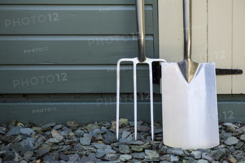 Garden fork and spade leaning against a painted shed
