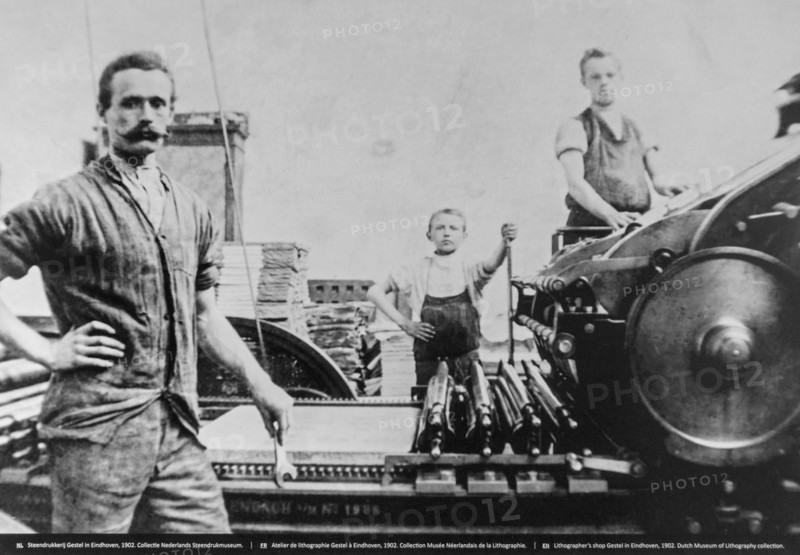 1902 black and white archival photo showing pressman and children working on lithographic printing press in pressroom