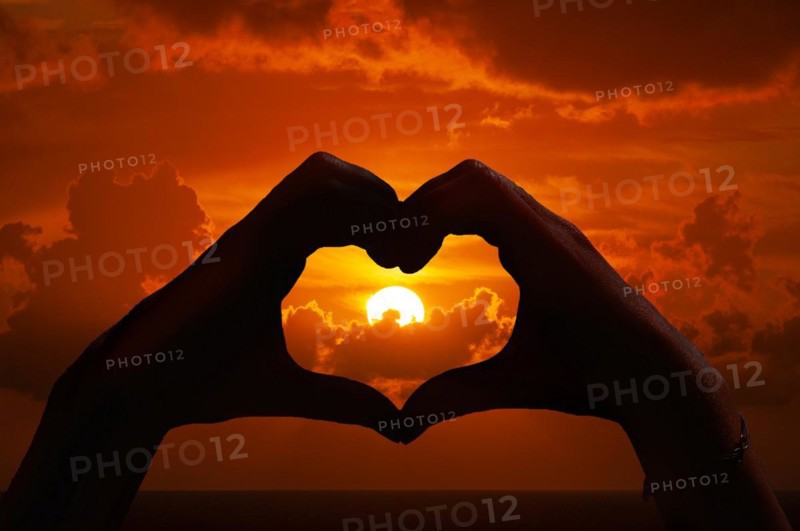 Hands form a heart in front of a sunset