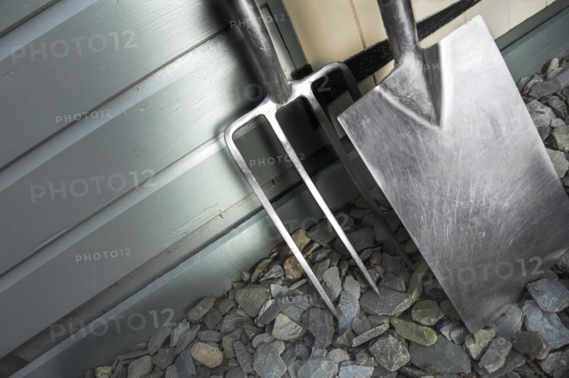 Garden fork and spade leaning against a painted shed