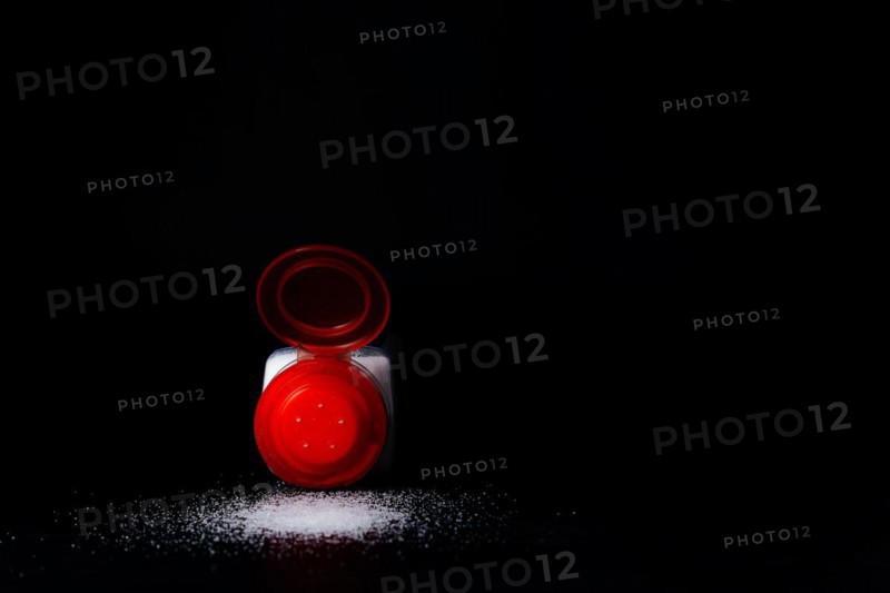 Close-up of a red salt shaker with spilled salt on a black table