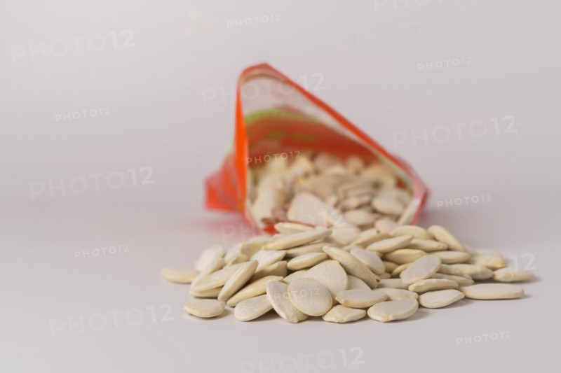 Roasted pumpkin seeds with salt coming out of their red bag on a white table with copy space