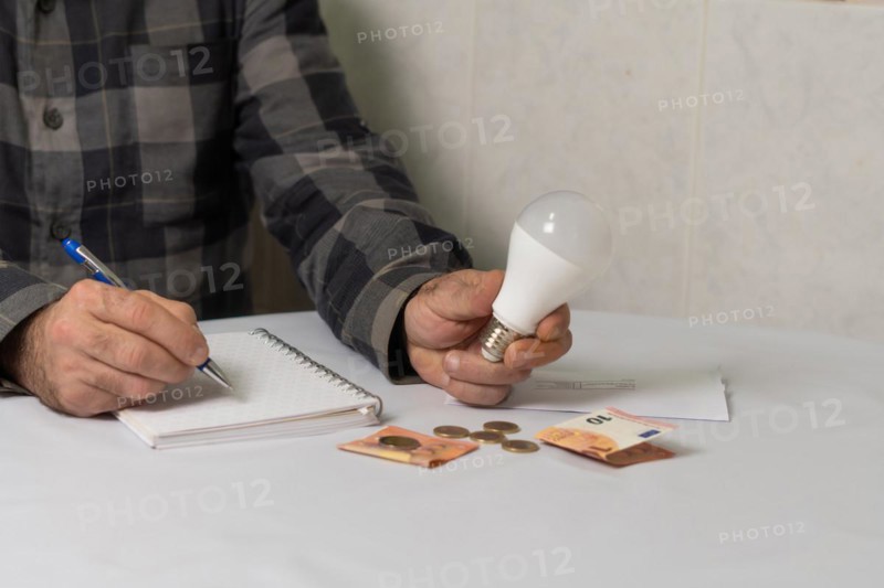 Man holding a light bulb writing down his expenses in a notebook