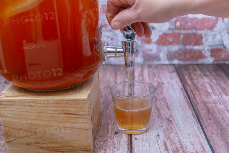 Woman's hand opening the tap of a bottle of home-made fermented kombucha tea