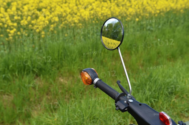 Rear view mirror of moped Schwalbe from the GDR in front of a rape field