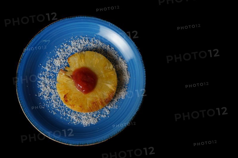 Close-up of a grilled natural pineapple with grated coconut on a blue plate on a black background