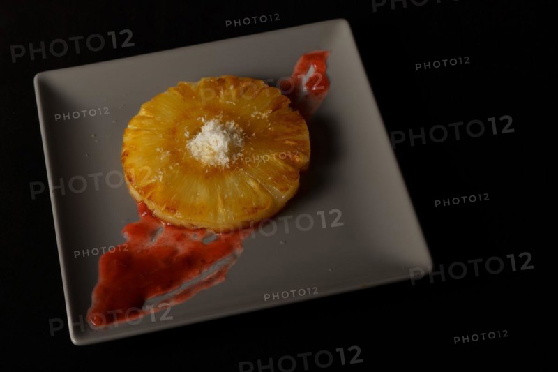 Close-up of a grilled natural pineapple with grated coconut on a grey plate on a black background