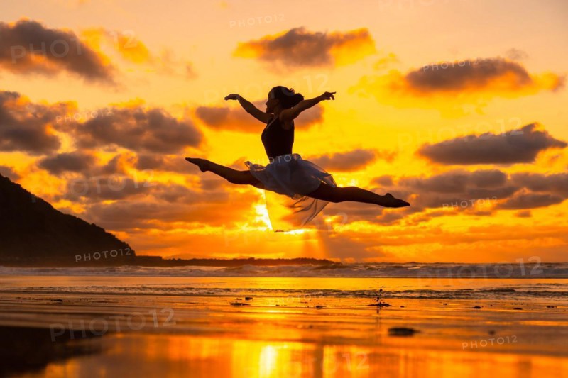 Young dancer on the beach at sunset performing a jump with the sea in the background