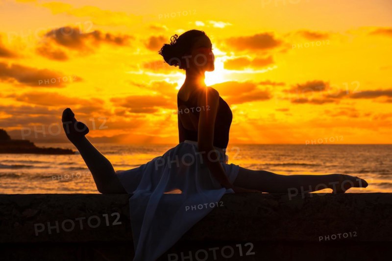 A young woman dancer by the beach at sunset doing spagata with the sea in the background