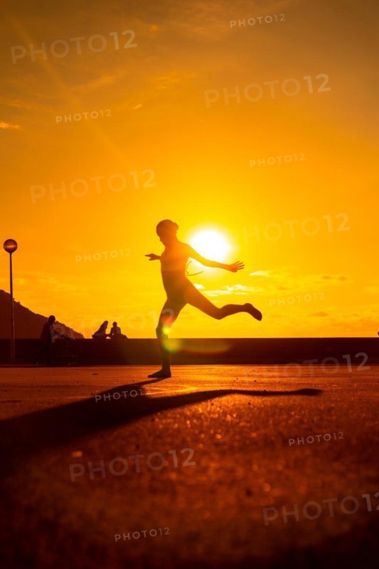 Silhouette of a young female dancer performing a jump along the beach at sunset