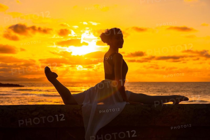 Silhouette of a young woman dancer next to the beach at sunset doing spagata with the sea in the background