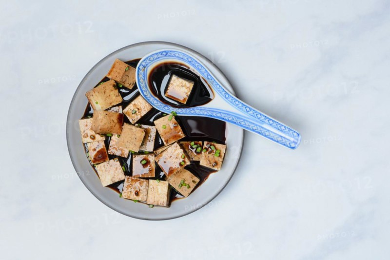 Soy sauce marinated tofu cubes in bowl with Asian ceramic spoon