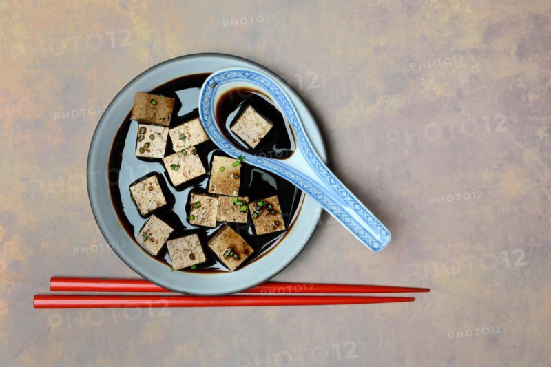 Soy sauce marinated tofu cubes in bowl with Asian ceramic spoon and chopsticks