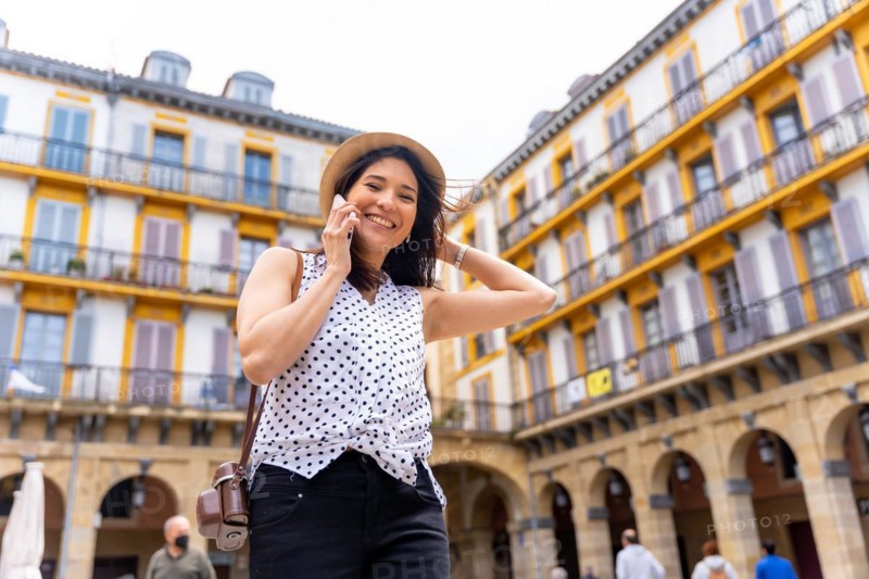 A woman in a hat visiting the city and talking on the phone
