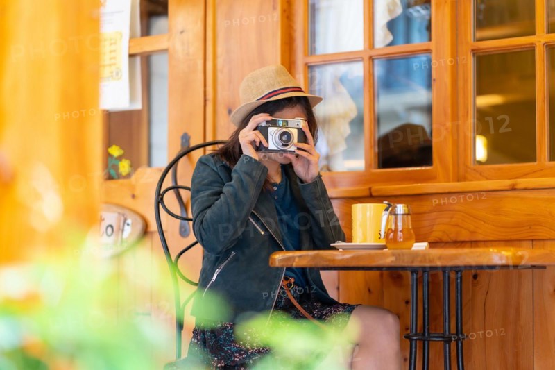 A tourist girl with a hat and a photo camera drinking tea on a cafe terrace