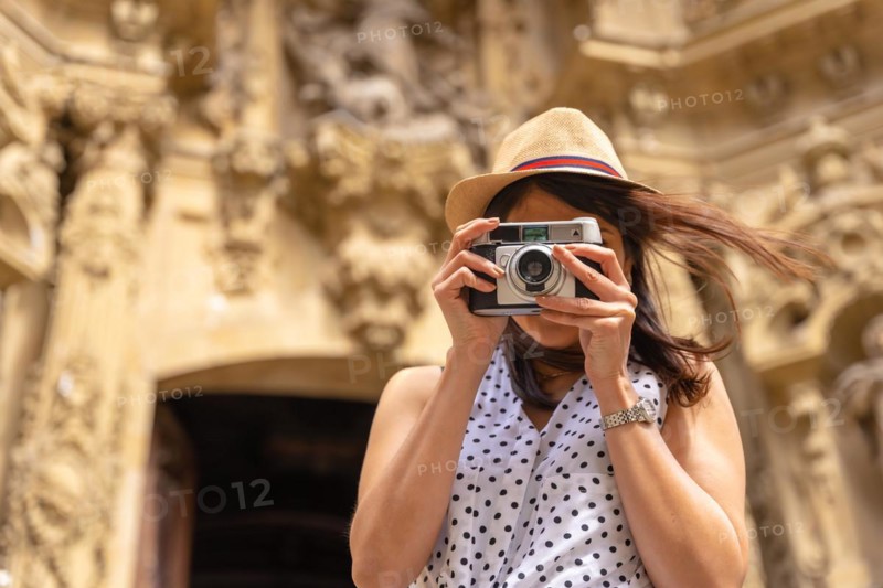 A woman in a hat visiting the city and taking photos with a vintage camera