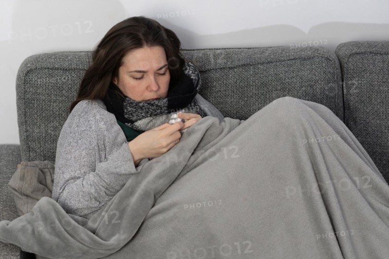 Sick woman taking fever pills covered with a blanket on the sofa in her home