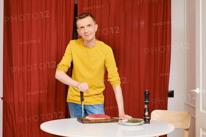 Middle-aged man leaning against knife and going to prepare duck breast